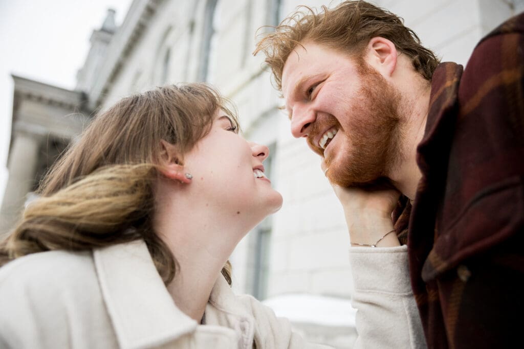 A bride touches her groom's cheek in downtown kingston with city hall behind them