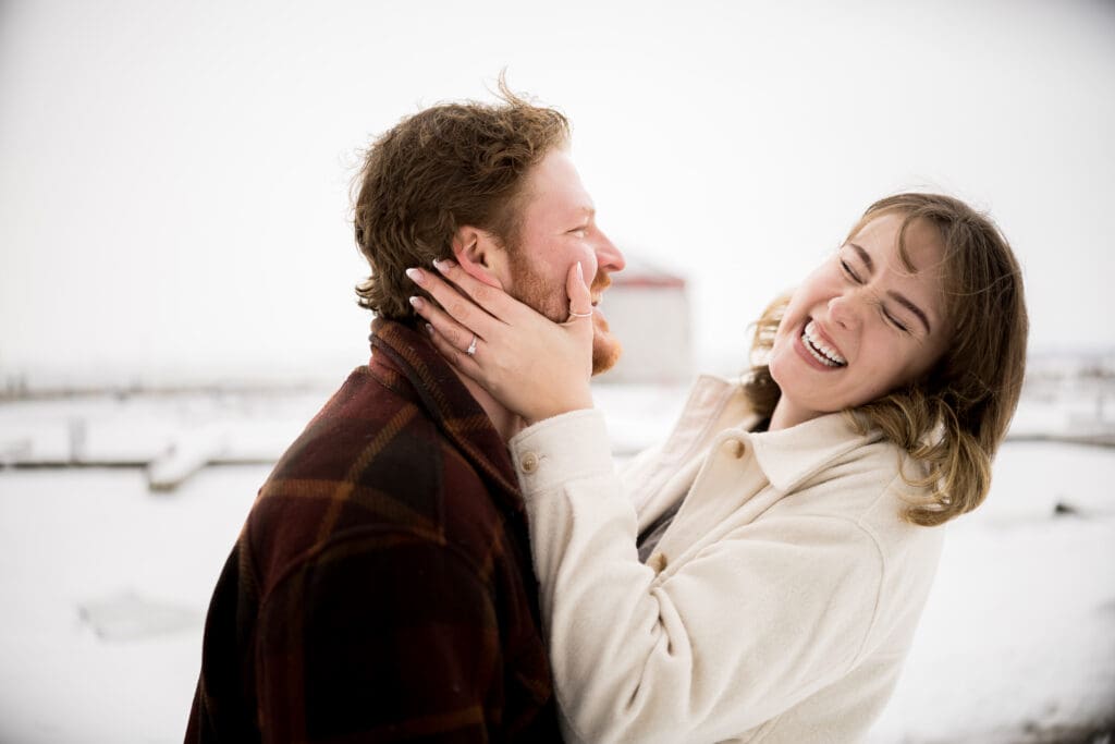 An engaged couple laughs in front of the St Lawrence River covered in ice and snow