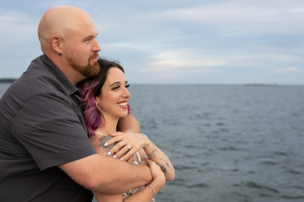 engaged couple smiling and looking out at the water
